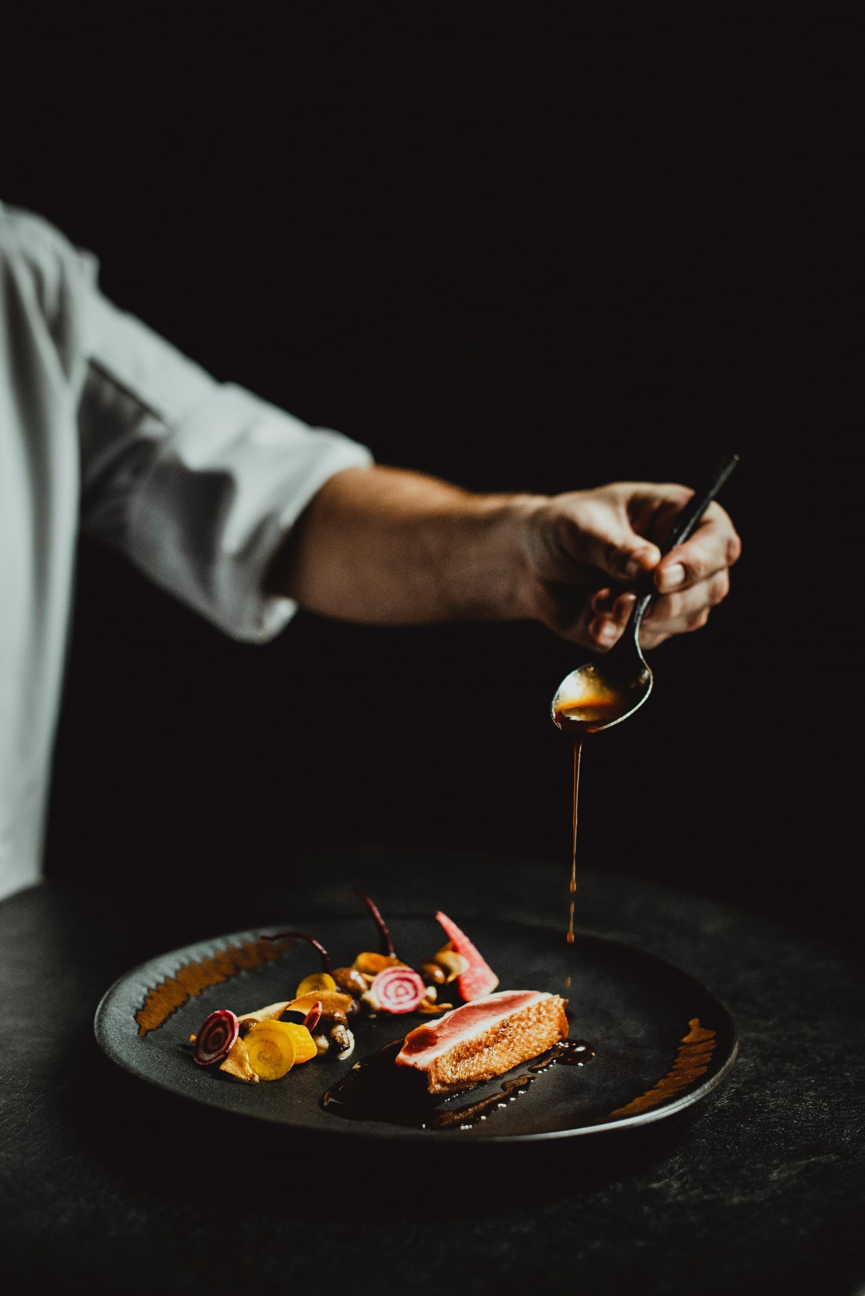 A chef finishing a plated dish with a delicate pour of jus
