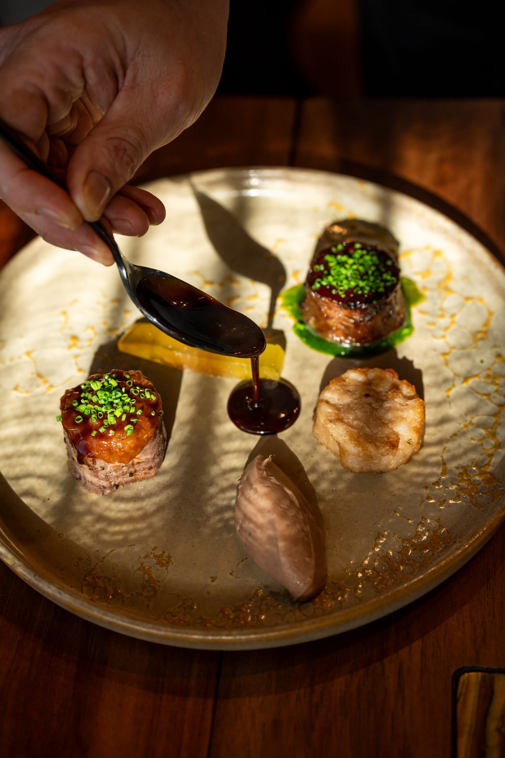 A chef spooning a dark sauce over a delicately plated course