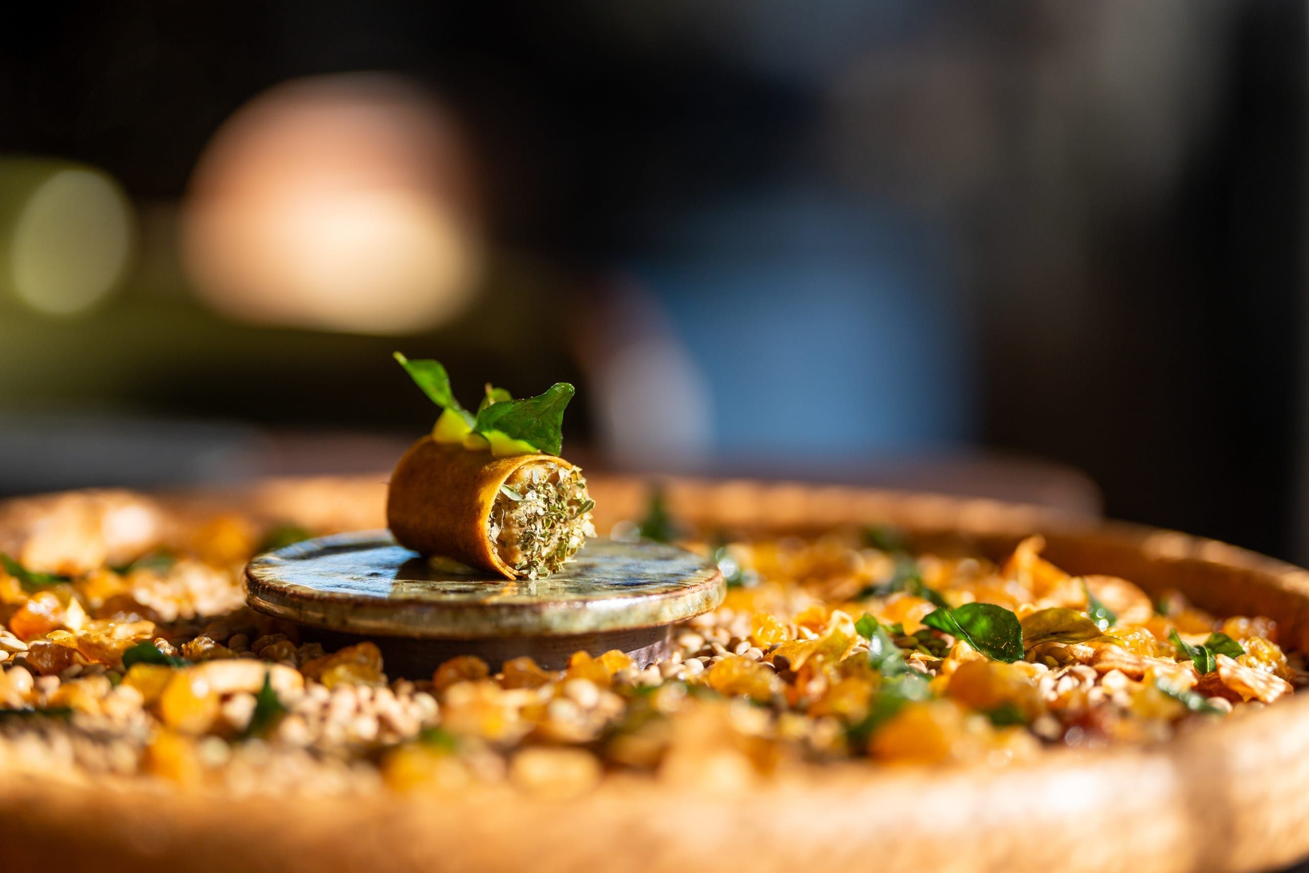 A delicate canapé presented on a stone disc above a bed of seeds and herbs