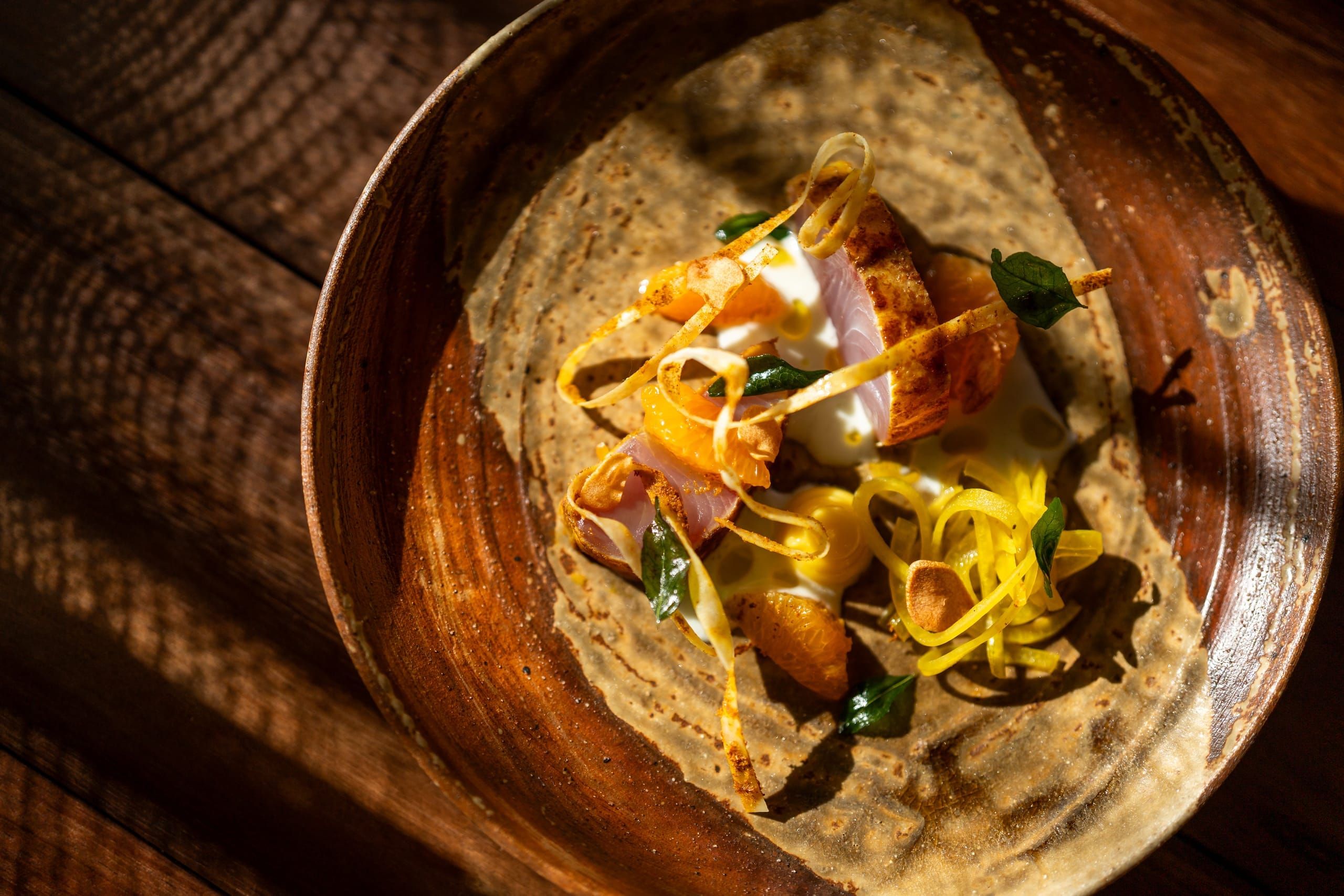 A delicate canapé presented on a stone disc above a bed of seeds and herbs