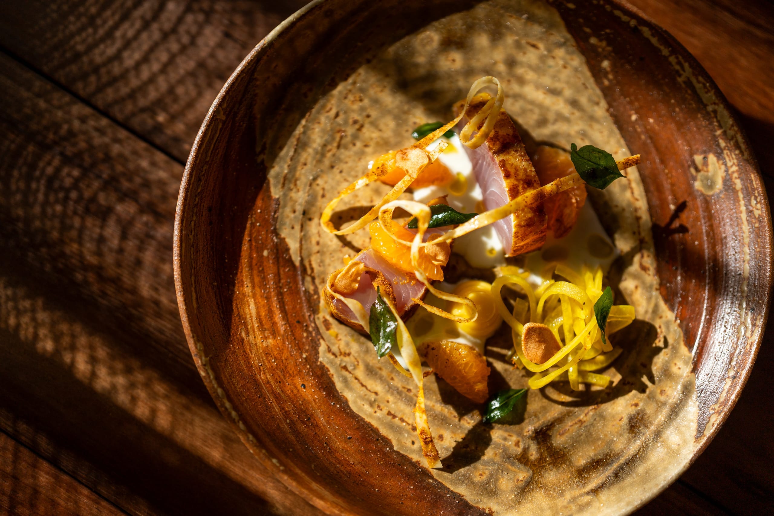 A delicate canapé presented on a stone disc above a bed of seeds and herbs