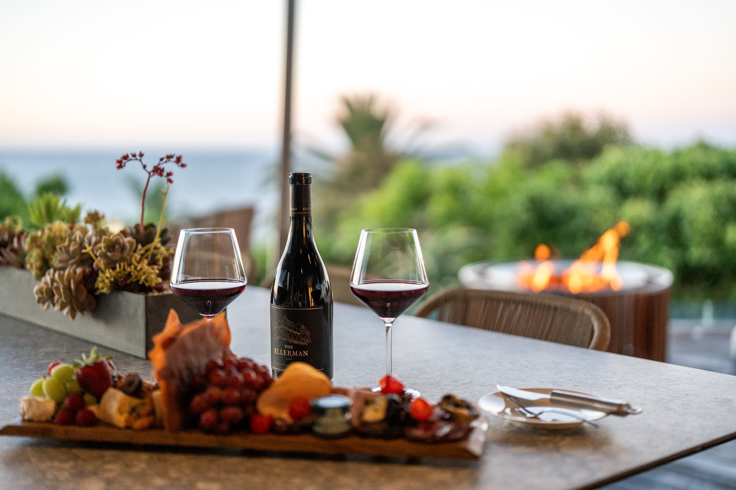 Red wine glass and bottle on a table outside by a fireplace