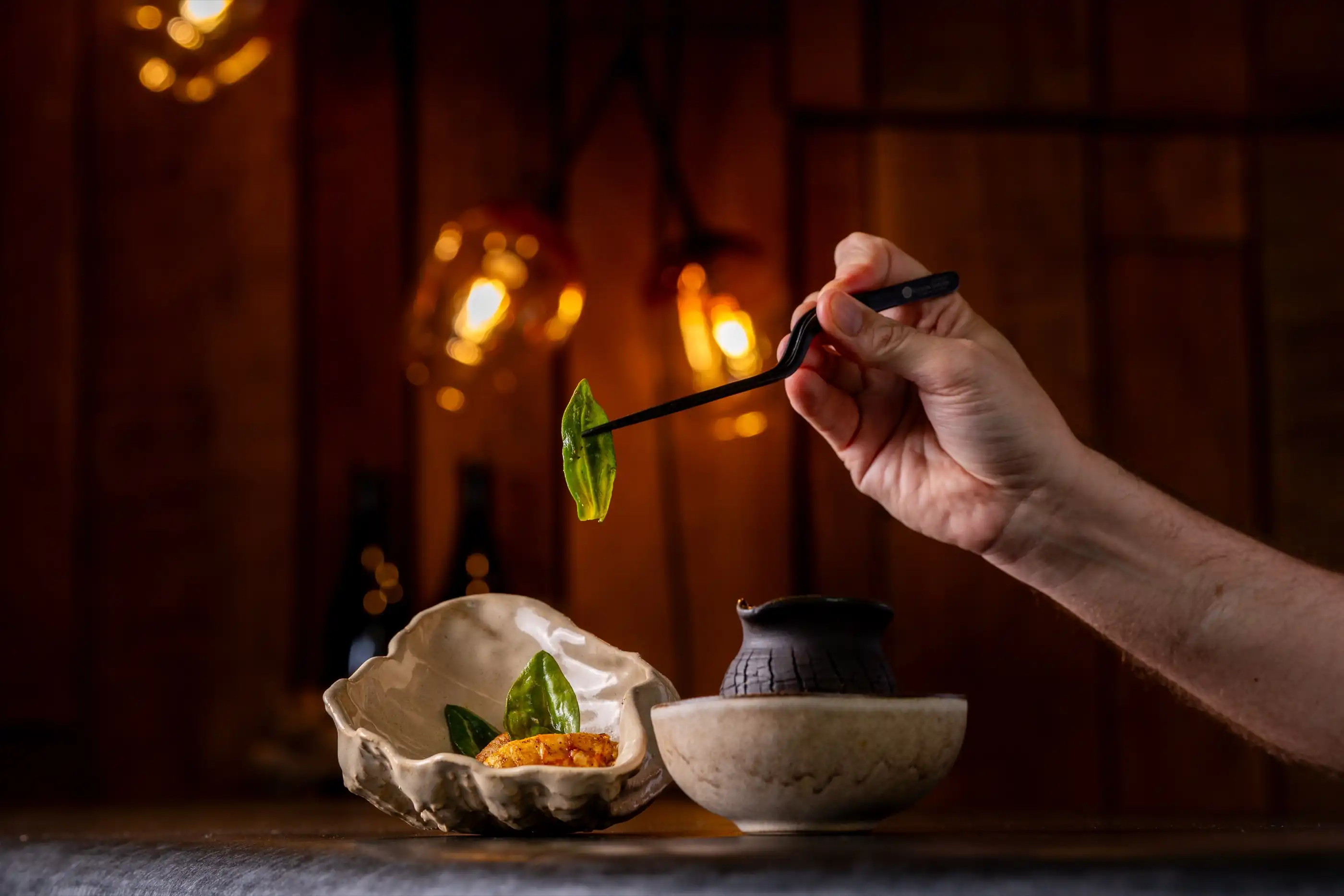 The chef plating a dish with tweezers under the kitchen light