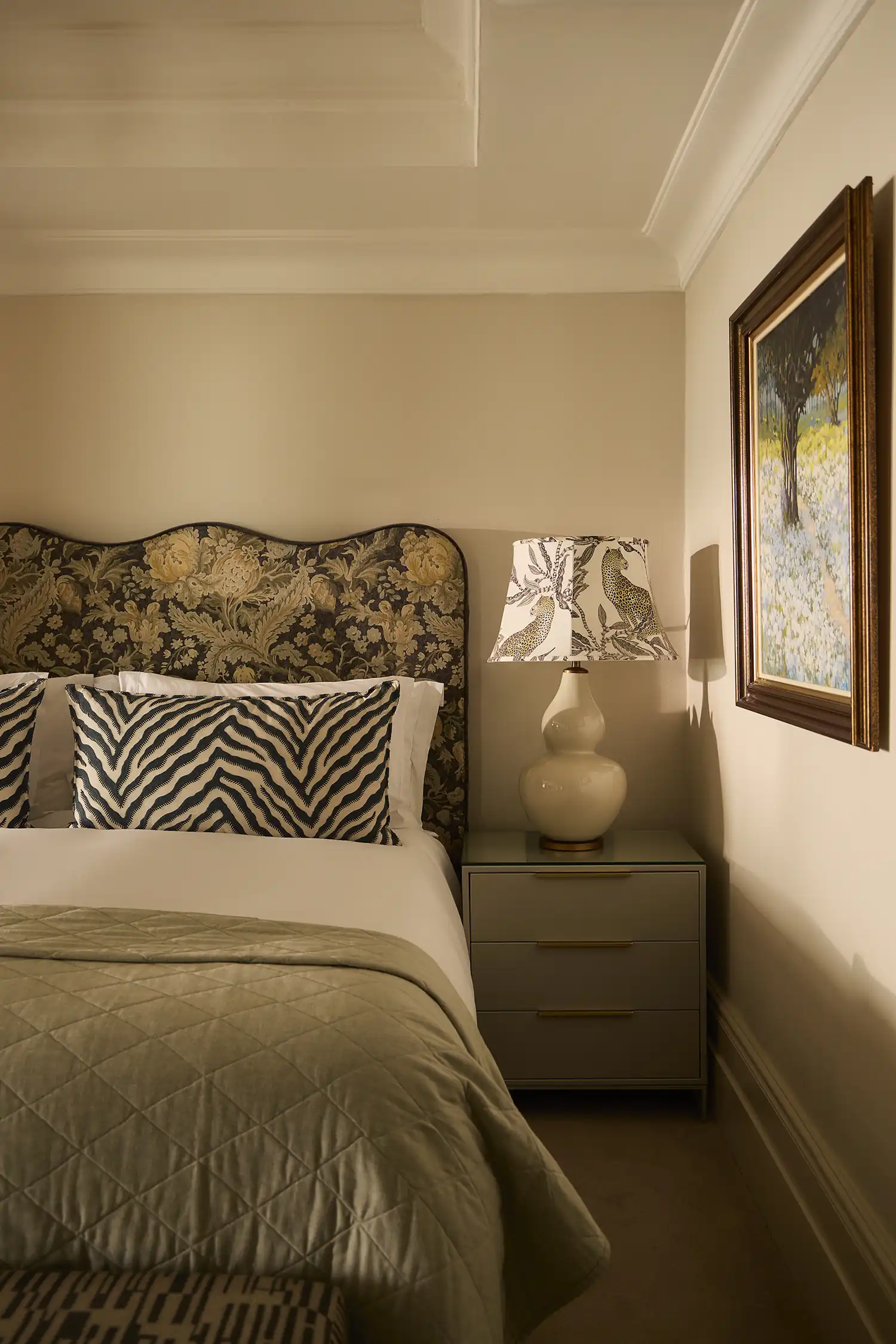 A bedroom with a patterned headboard beneath an original painting