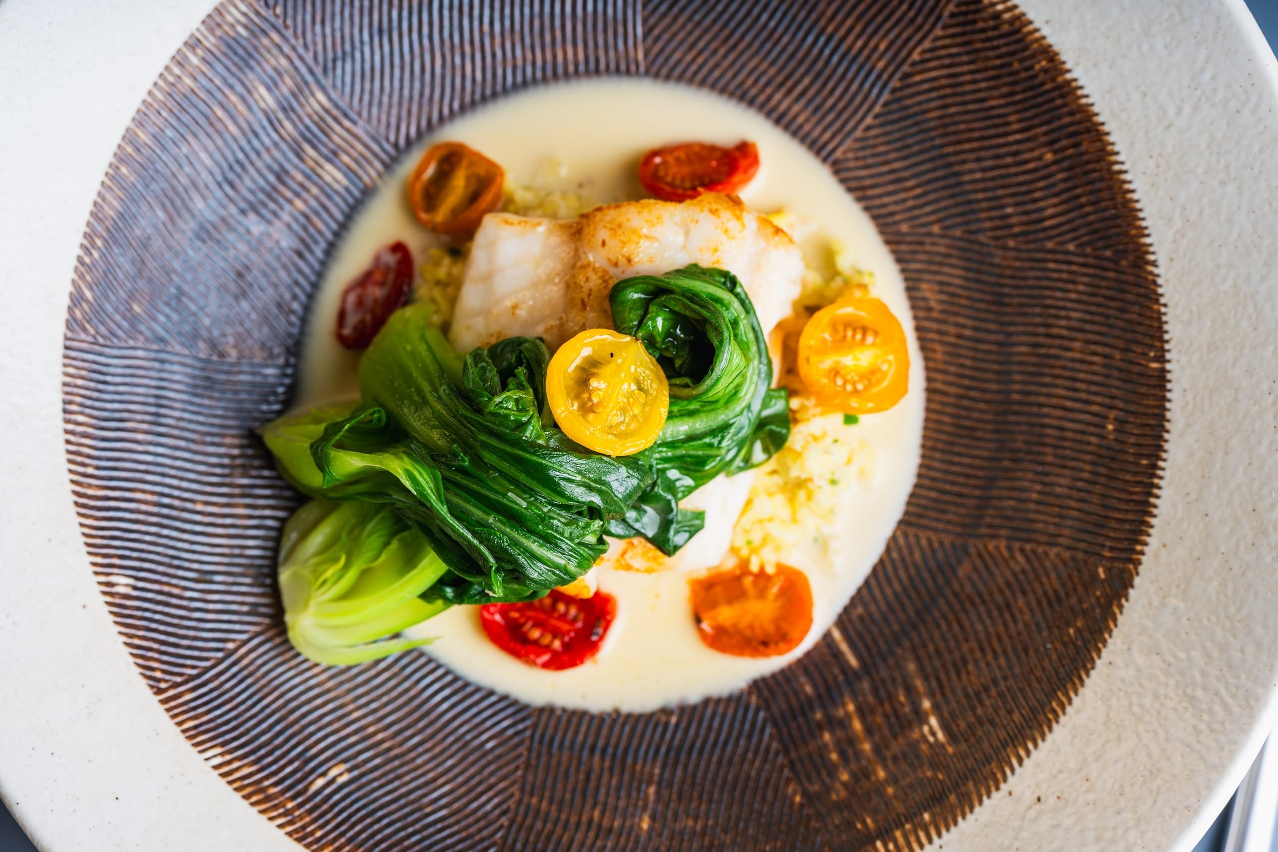 A delicate fish course with bok choy and cherry tomatoes in a creamy sauce, viewed from above