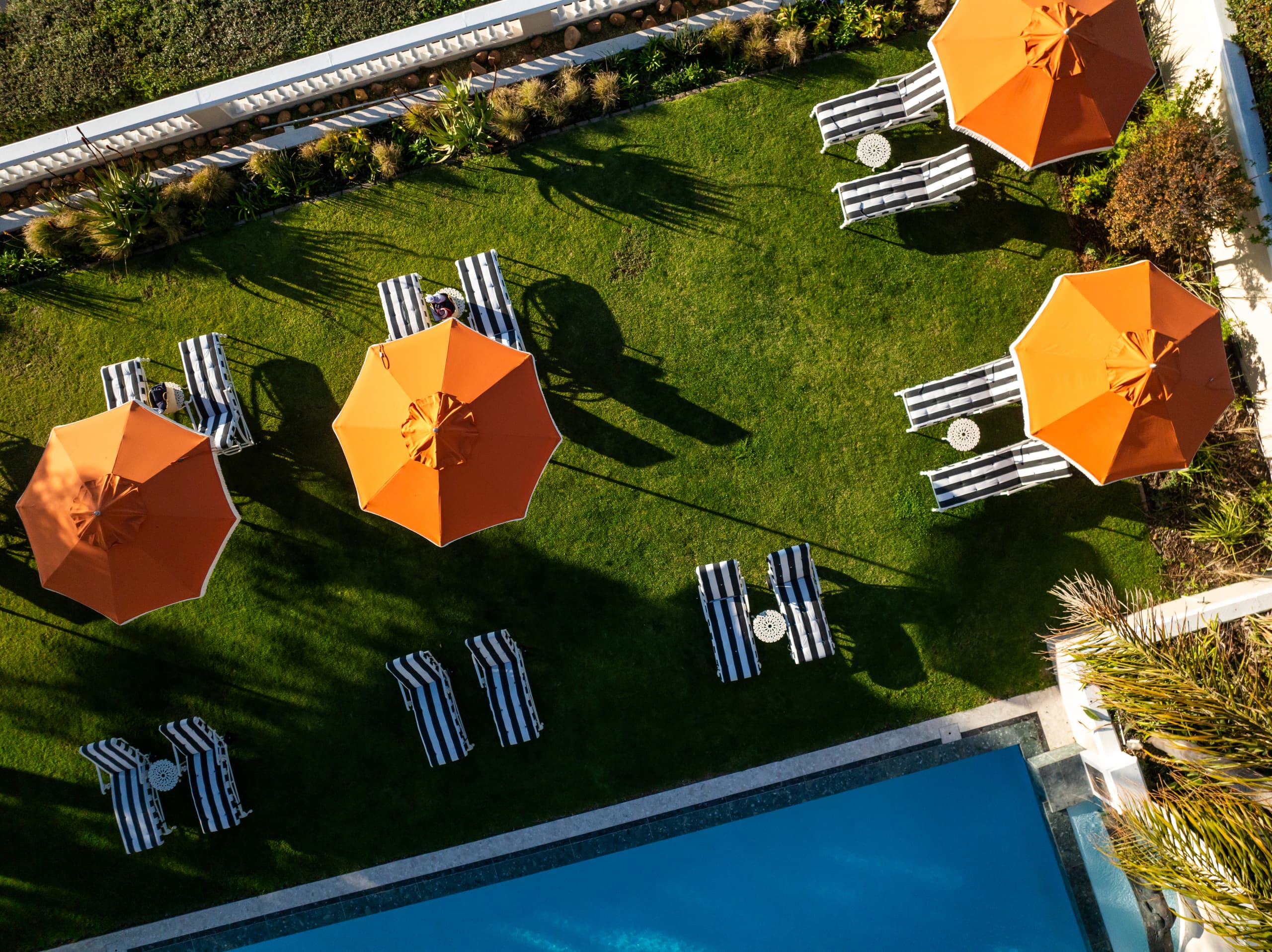 An aerial view of the pool, lawn and striped loungers beneath orange umbrellas